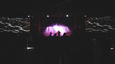 Silhouetted band performing on stage with purple backlighting in a dark venue.