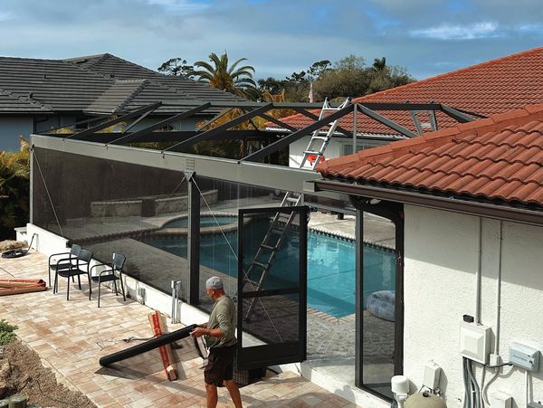 Man working on pool cage under a cloudy sky.