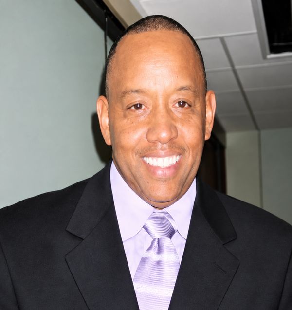 Smiling man in a suit and lavender tie.
