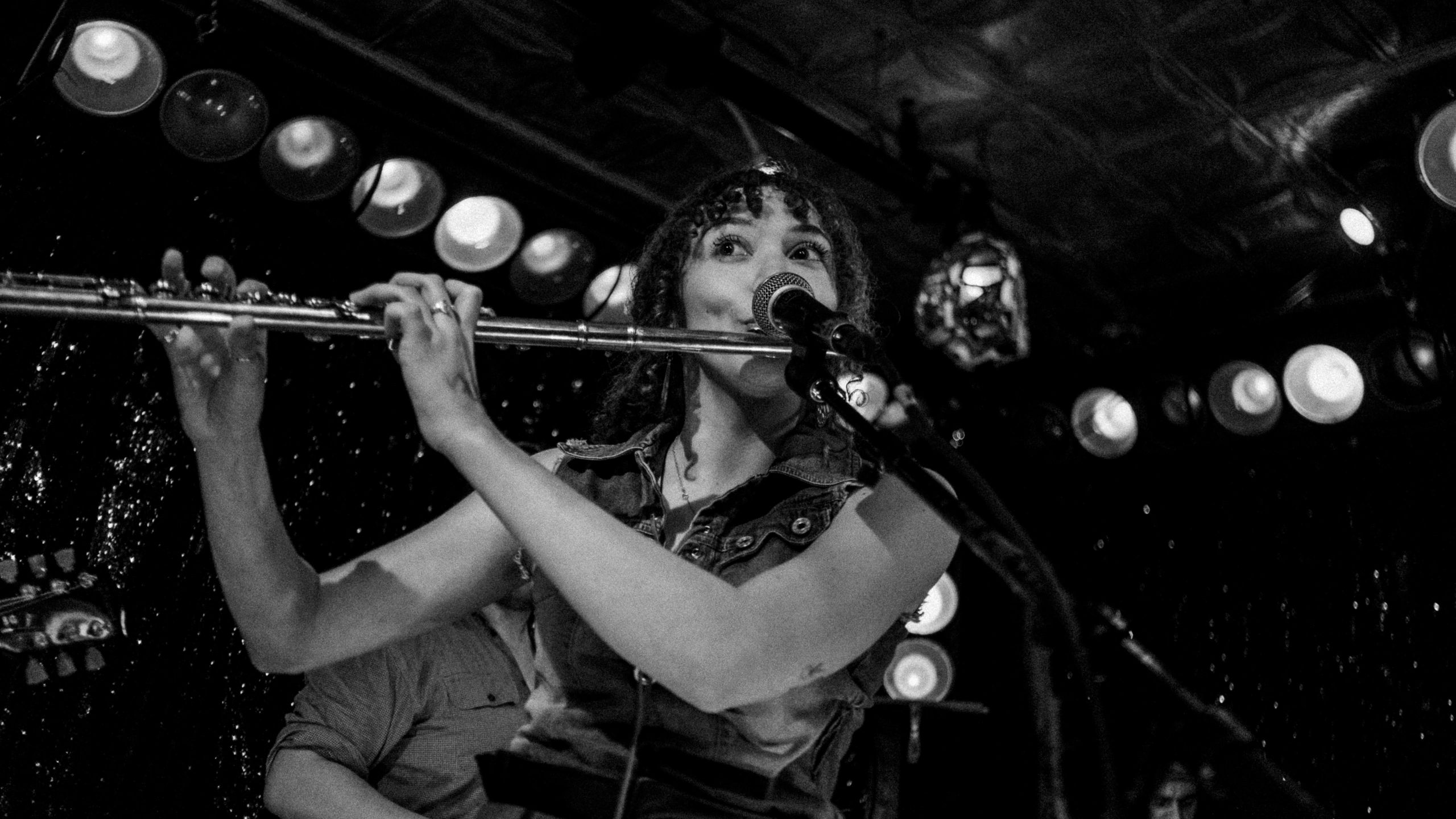 Musician playing flute and singing into microphone on stage.