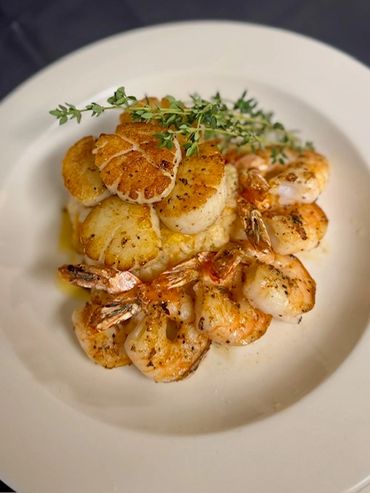 Grilled shrimp and scallops garnished with fresh herbs on a white plate.
