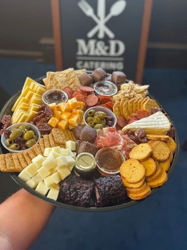 A colorful charcuterie platter with cheeses, crackers, meats, olives, and dips.
