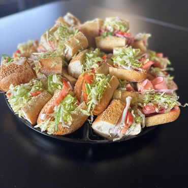 A plate piled with assorted mini sandwiches filled with lettuce and tomatoes.