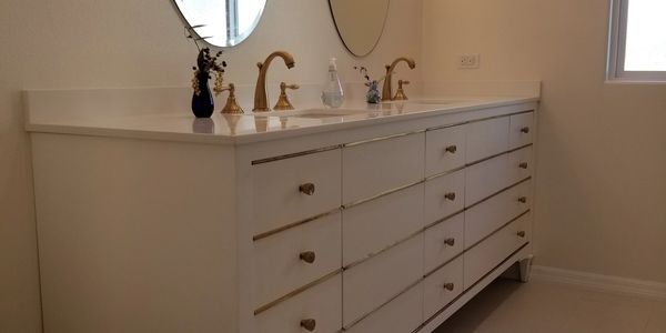 Modern bathroom vanity with gold fixtures and oval mirrors.
