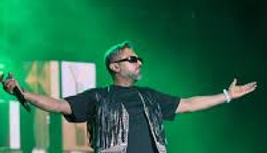 Performer on stage with arms outstretched under green lighting.