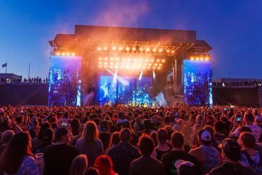Large crowd at an outdoor concert with bright stage lights.