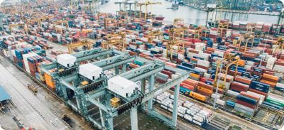 Cargo containers stacked at a busy port with cranes.