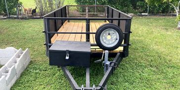 Empty utility trailer with wooden floor parked on grass.
