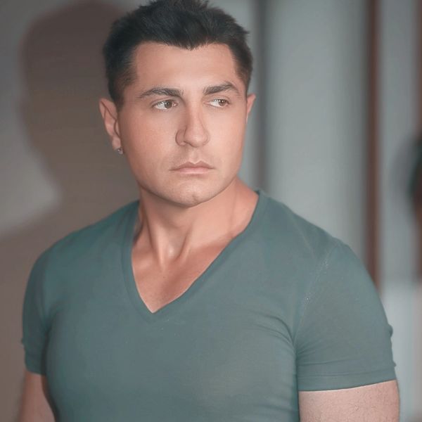 A man in a teal V-neck shirt looking to the side with a serious expression.
