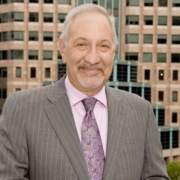 Smiling older man in a pinstripe suit and paisley tie outdoors.