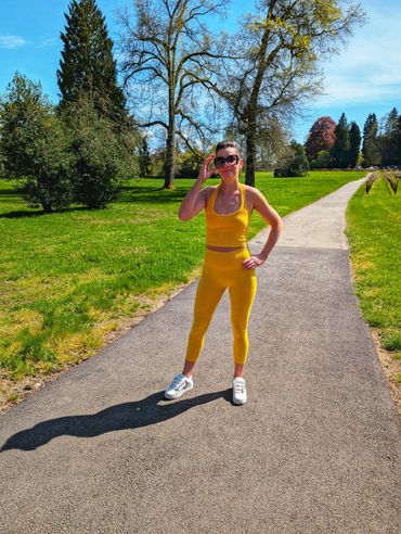 Woman in yellow workout clothes standing on a park path on a sunny day.