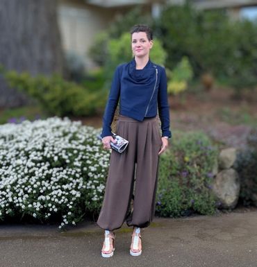 Woman in stylish outfit posing outdoors near flowers and greenery.