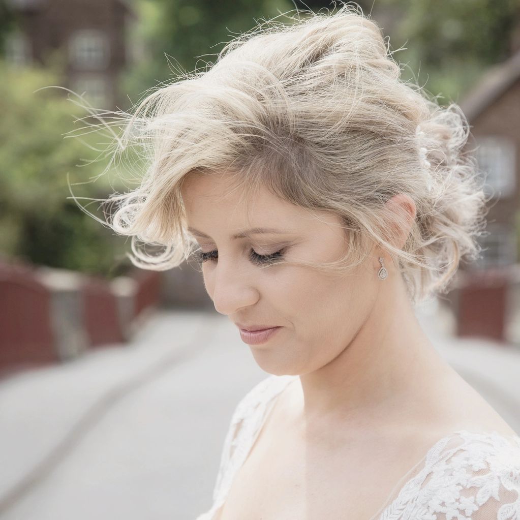 A serene woman with blonde hair and delicate lace dress smiles softly outdoors.