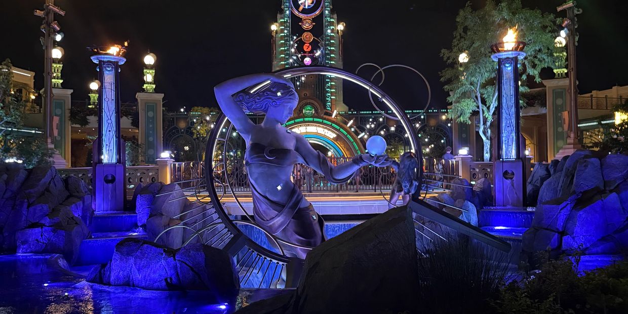 Illuminated statue of a woman with a glowing orb at night in a decorative fountain.