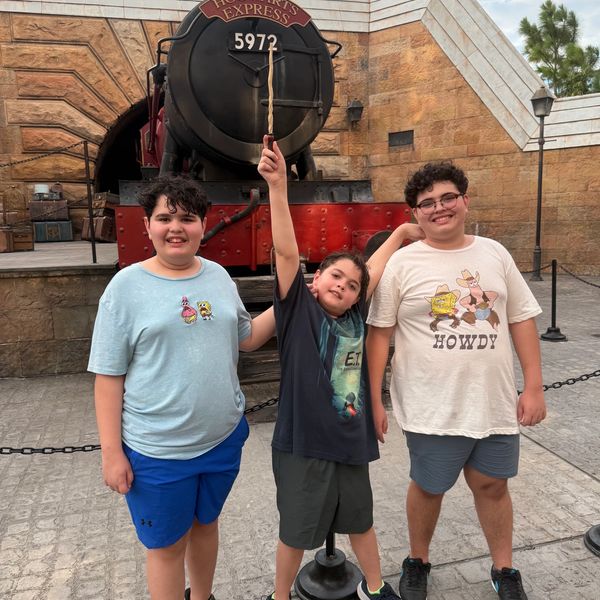 Three boys posing happily in front of the Hogwarts Express train.