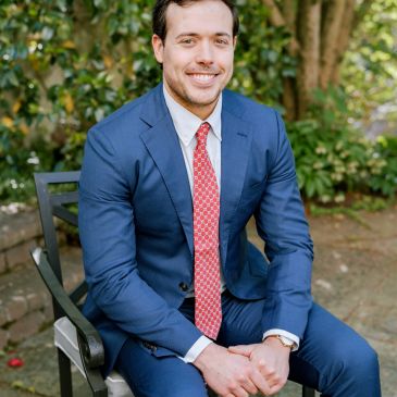 Man in blue suit sitting outdoors on a chair.