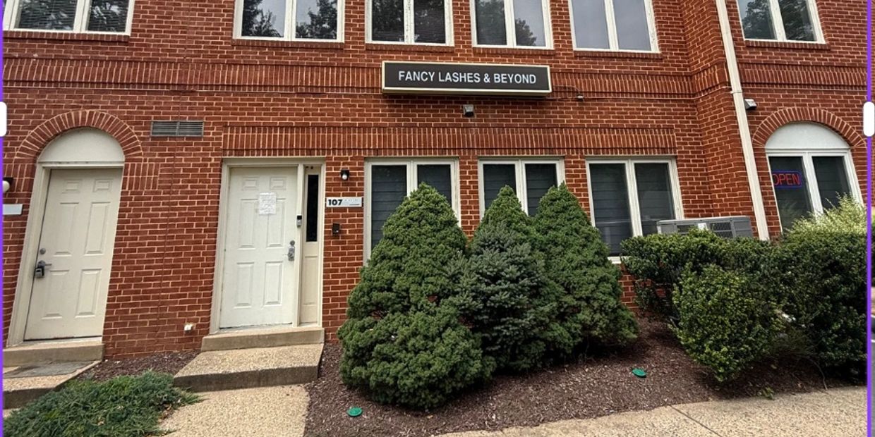 Brick building with sign "Fancy Lashes &amp; Beyond" and bushes outside.