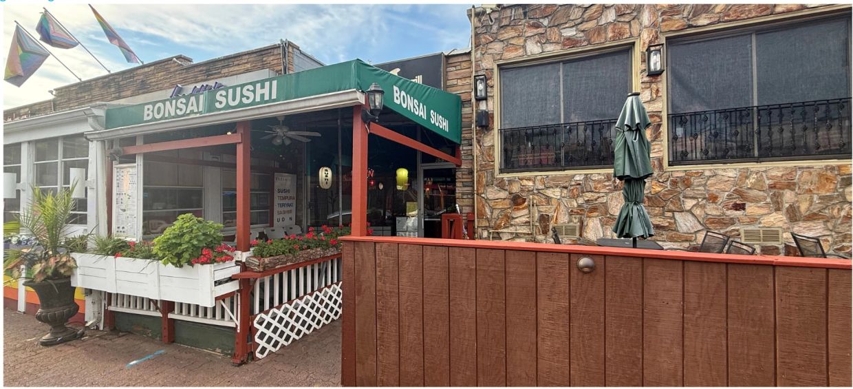 Entrance of Bonsai Sushi restaurant with green awning and outdoor plants.