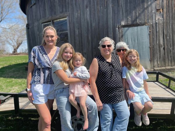 Photo of 6 people leaning against a trailer in front of a barn wall