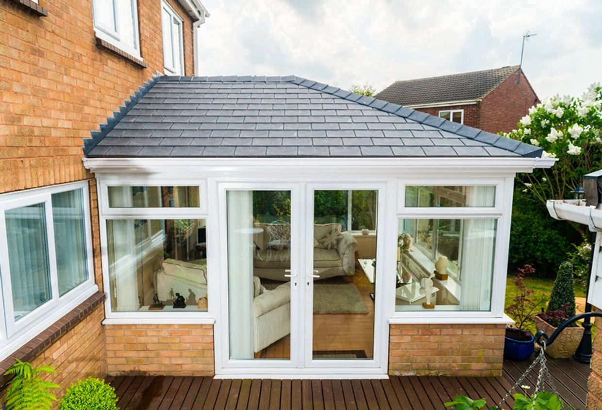 A cozy conservatory with large glass doors and windows attached to a brick house.