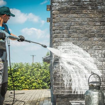 Man pressure washing a brick wall outdoors on a sunny day.