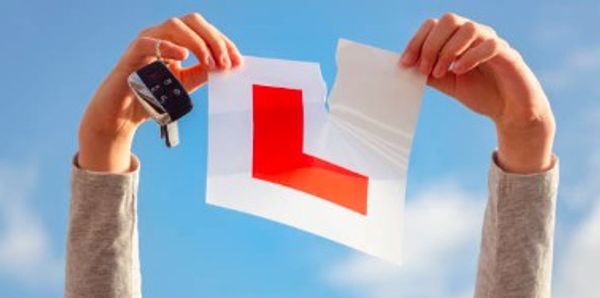 Person holding a torn learner driver L-plate and car keys against a blue sky.