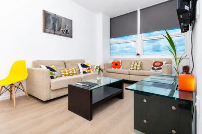 Bright modern living room with beige sofas and colorful cushions.