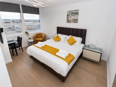 Modern hotel room with king bed and mustard accents.