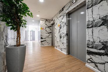 Modern hallway with two elevators, marble walls, and wooden flooring.