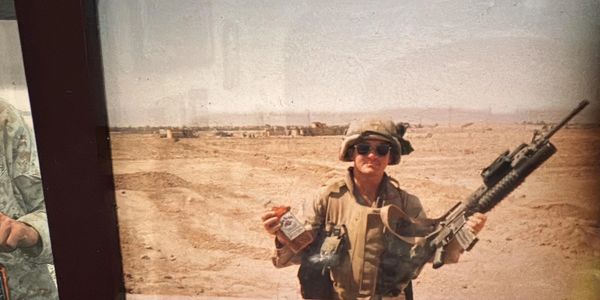 Soldier in desert holding a bottle and a rifle.