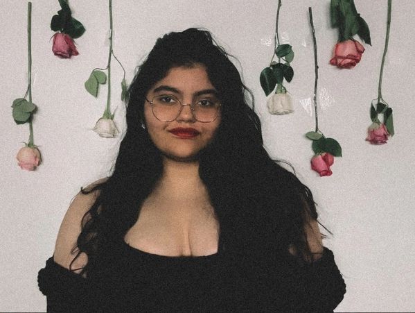 Woman with glasses and red lipstick posing before hanging roses.