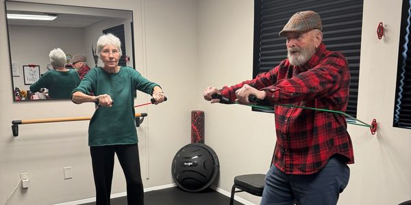 Two elderly individuals exercising with resistance bands in a fitness room.