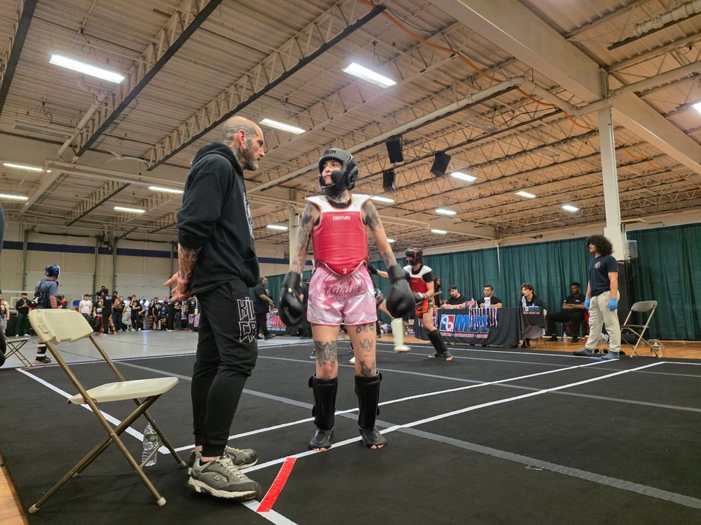 A coach talks to a female kickboxer in protective gear before a match.