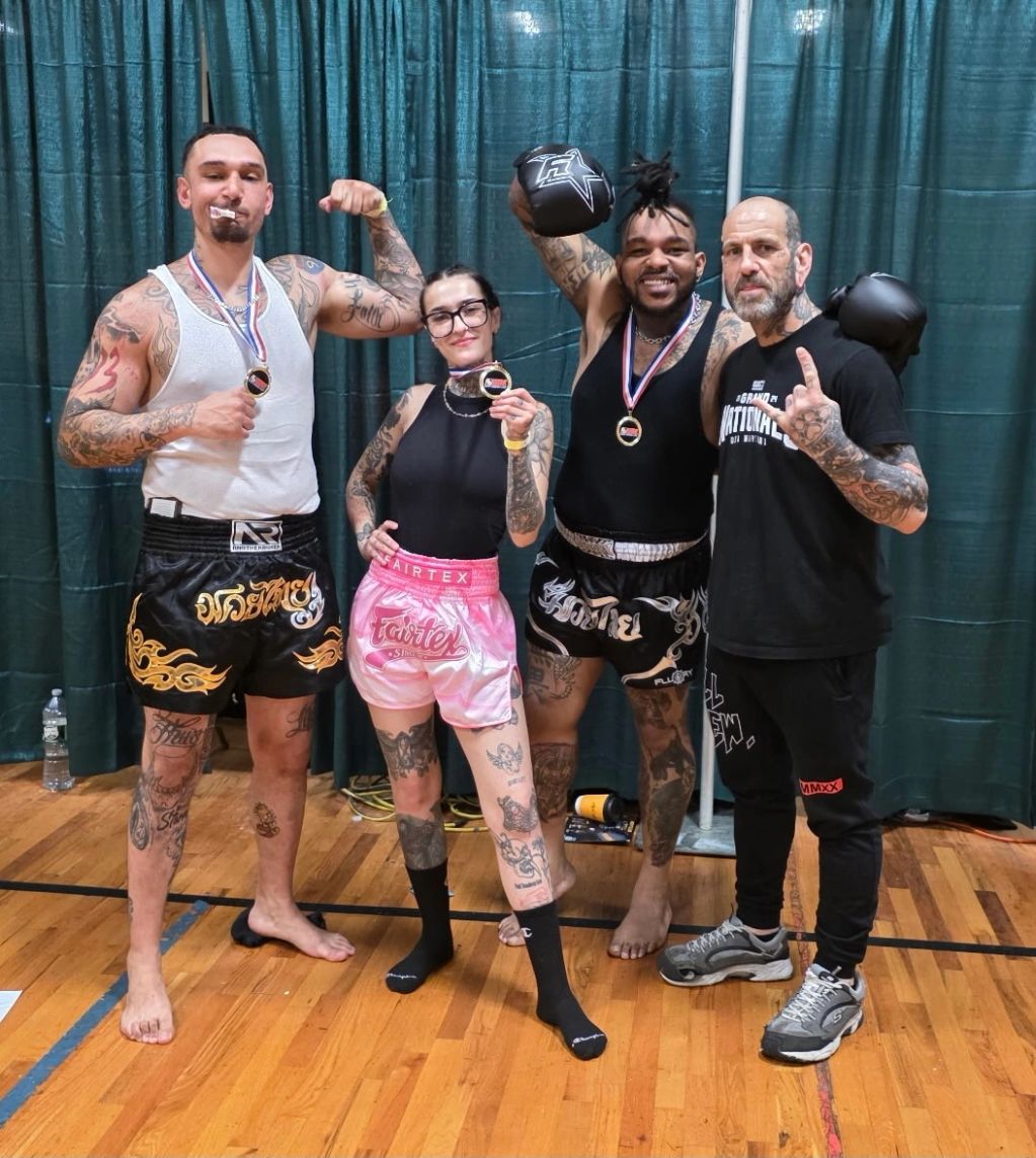 Four tattooed fighters proudly show their medals and boxing gloves after a match.