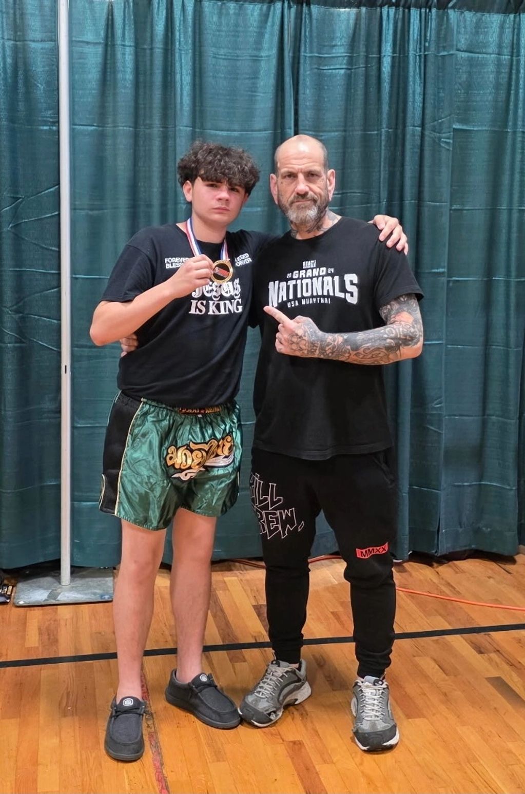 Two men posing in a gym, one holding a medal.