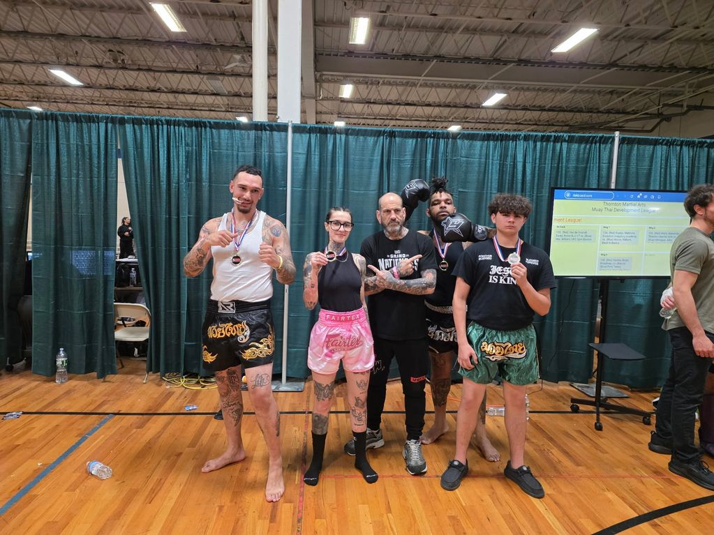 Five people posing in a gym, some wearing medals and Muay Thai shorts.