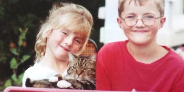 Two children happily holding a content tabby cat outdoors.