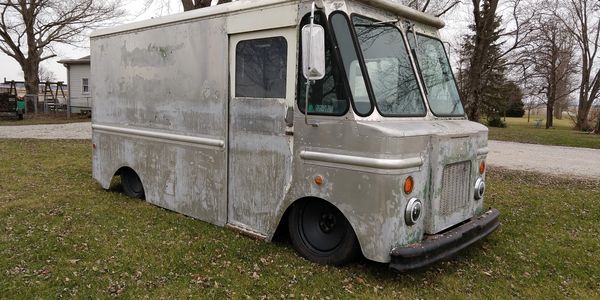 An old, rusty delivery truck with flat tires sitting on grass.