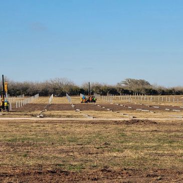 A large construction site with foundation posts and machinery under clear blue sky.