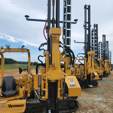 A row of yellow Vermeer drilling machines on a dirt field under a cloudy sky.
