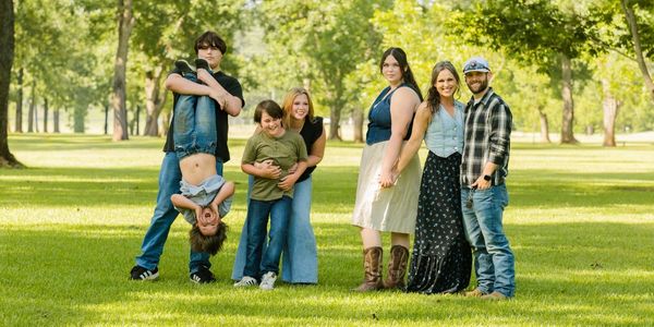 A family posing playfully in a sunny park with greenery.