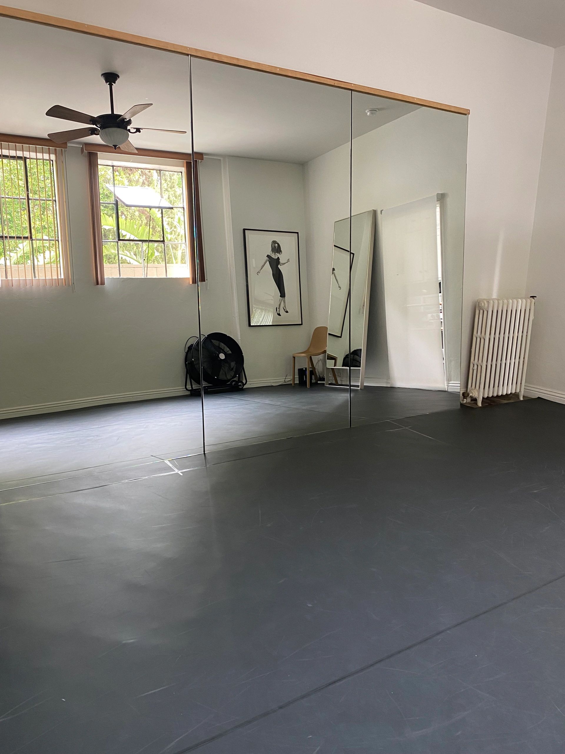 Bright dance studio with mirrored wall, fan, and minimal decor.