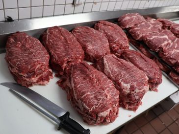 Several large raw beef steaks lined up on a countertop with a knife.