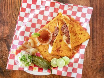 A savory quesadilla with sides of lime, pickled vegetables, and dipping sauce.