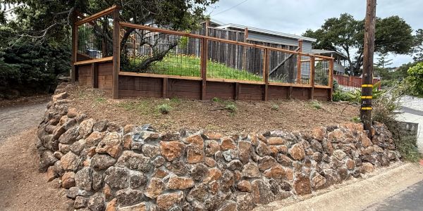 Stone retaining wall with wooden fence on top enclosing grassy area.