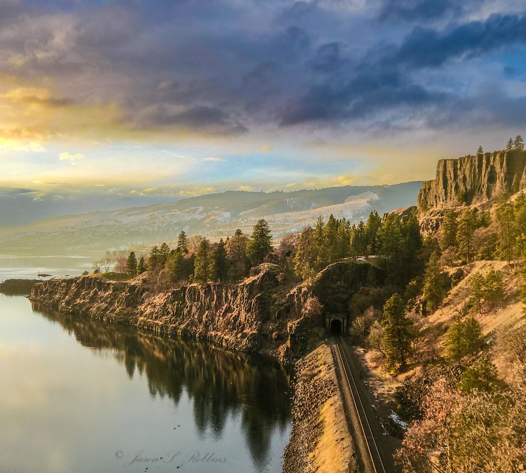 Railroad tracks disappear into the hillside along the river at sunset. 