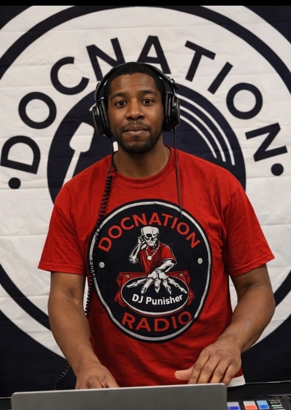 DJ Punisher wearing a red DOCNATION RADIO shirt with headphones on.