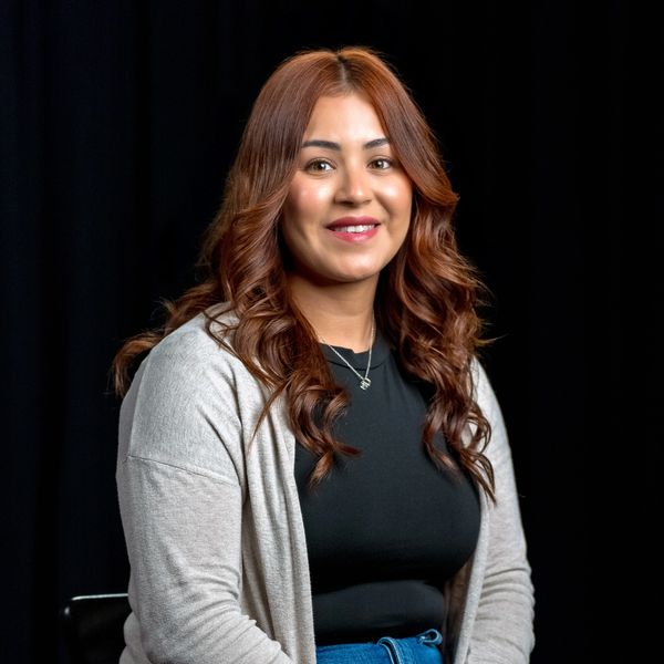 Smiling woman with wavy hair in casual attire against a black background.