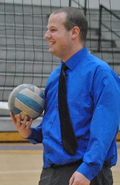 Smiling man in blue shirt holding a volleyball indoors.