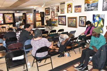 A small group of people sitting on folding chairs in an art gallery.